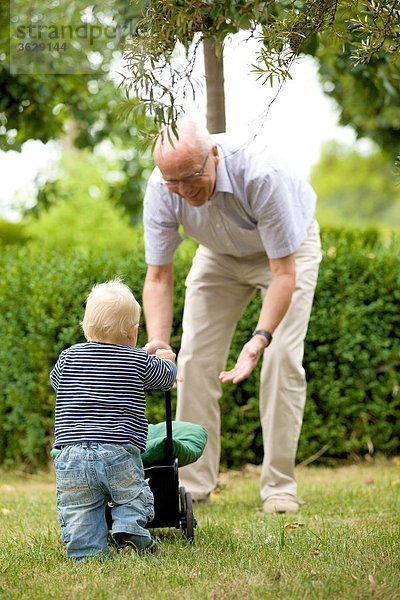 Großvater und Kleinkind mit Puppenwagen im Freien