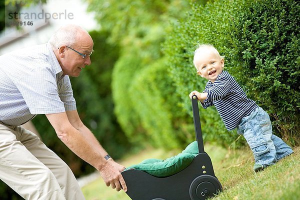 Großvater und Kleinkind mit Puppenwagen im Freien