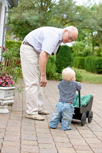 Großvater und Kleinkind mit Puppenwagen im Freien