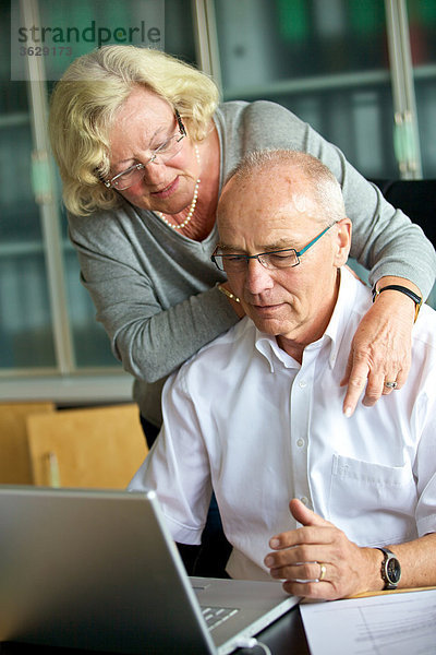 Seniorin umarmt Mann am Schreibtisch