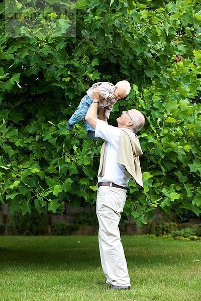 Großvater hebt Kleinkind im Freien hoch