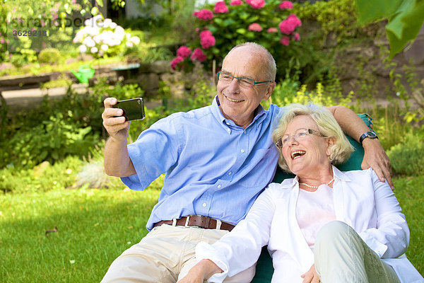 Glückliches Seniorenpaar mit Smartphone im Garten