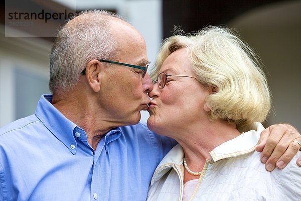 Seniorenpaar küsst sich vor Wohnhaus
