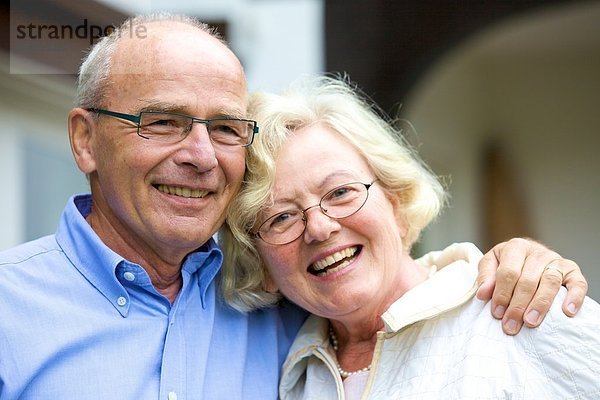 Glückliches Seniorenpaar umarmt sich vor Wohnhaus  Portrait