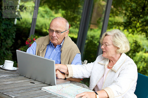 Seniorenpaar auf der Terrasse mit Laptop und Straßenkarte