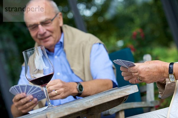 Seniorenpaar spielt Karten und trinkt Rotwein