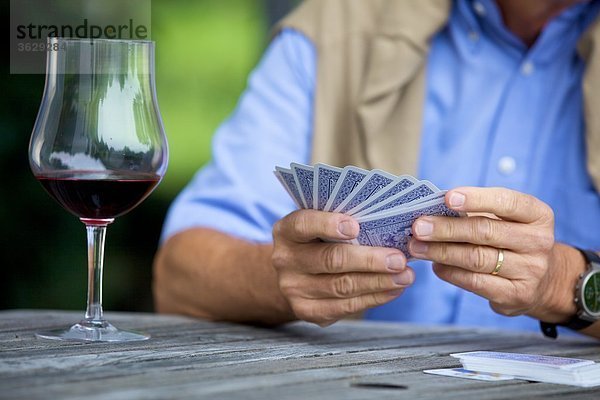 Senior spielt Karten und trinkt Rotwein  close-up