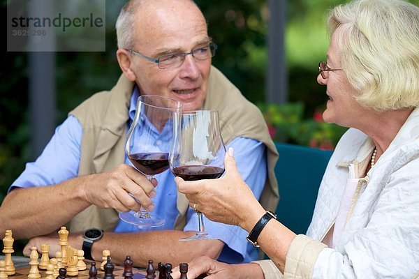 Seniorenpaar auf der Terrasse spielt Schach und trinkt Rotwein