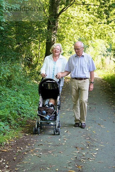 Großeltern gehen mit Enkelsohn im Kinderwagen spazieren
