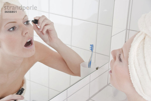 Frau beim Tuschen der Wimpern im Bad vor dem Spiegel
