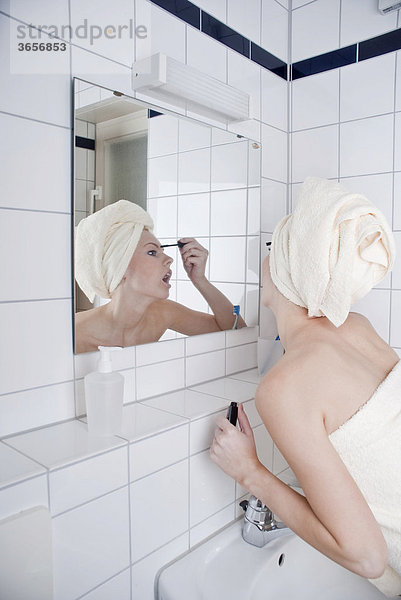 Frau beim Tuschen der Wimpern im Bad vor dem Spiegel