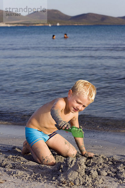 Ein Junge  5 Jahre  an einem Sandstrand  buddelt im Sand