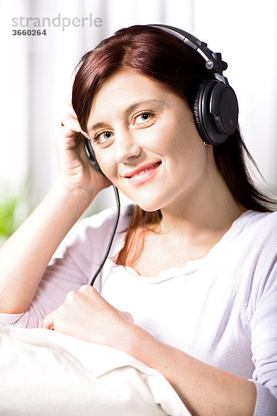 Junge Frau hört Musik über Kopfhörer im Wohnzimmer