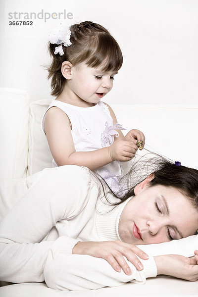 Kleines Mädchen spielt mit dem Haar der schlafenden Mutter
