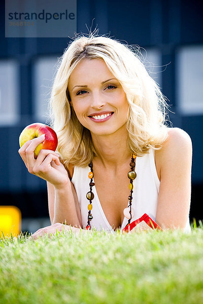 Junge Frau mit Apfel auf der Wiese