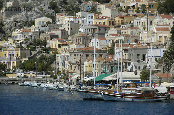 Blick auf die farbenfrohen ockerfarbenen Häuser mit Segelbooten im Hafen der Insel Symi Griechenland