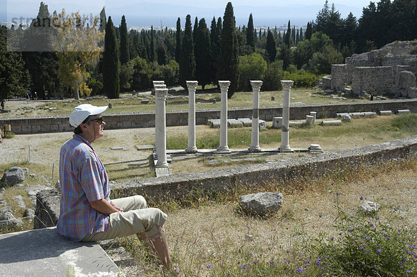 Antikes Griechenland aktive Senioren Frau sitzt vor einer Reihe von Säulen vor Wald aus schlanken Zypressen Asklepieion Insel Kos Griechenland