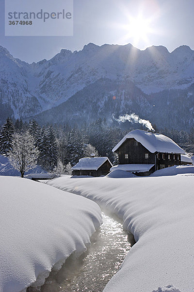 Altes Holzhaus an einem Bach in der tief verschneiten Landschaft dahinter das Grimming Massiv Krungl Steiermark Österreich Holzhaus