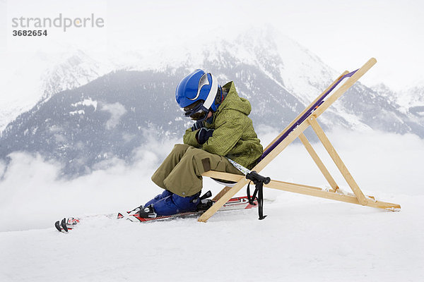 Kind mit Skiern auf Liegestuhl sitzend