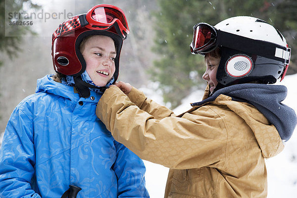 Kleiner Junge hilft Mädchen beim Skihelm machen