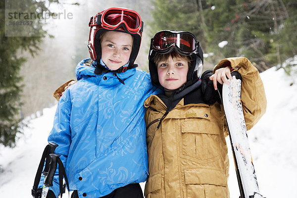 Kleine Kinder  die sich mit Skiern im Schnee umarmen