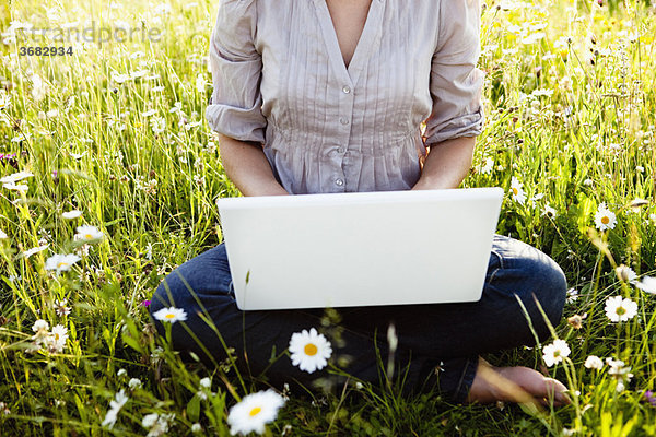 Frau mit Laptop auf wilder Wiese sitzend