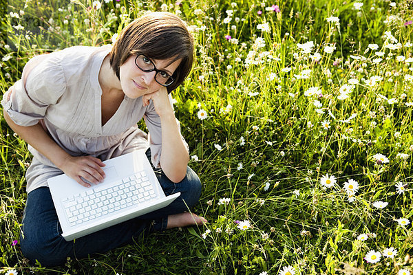 Frau mit Laptop auf wilder Wiese