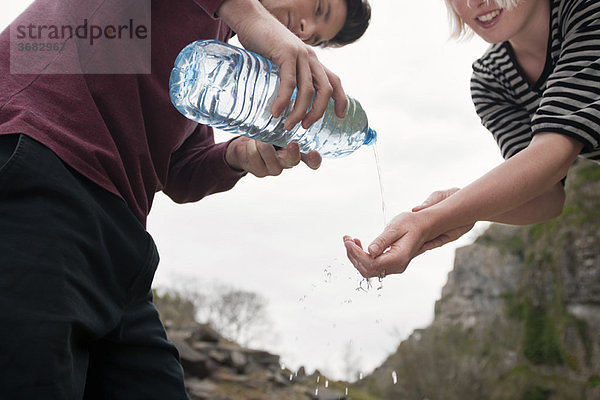 Mann gießt Wasser auf Frauenhände