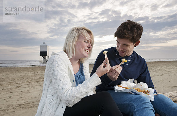 Pärchen am Strand essen Fisch und Pommes frites