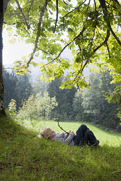 Junge  der mit einem Glied unter einem Baum spielt.