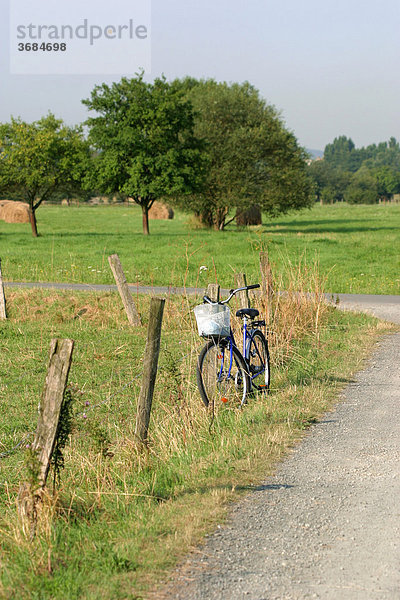 Ein Fahrrad lehnt an einem Weidezaun am Rande eines Weges