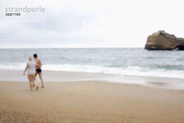 Ein Paar  das am Strand spazieren geht  defokussiert.