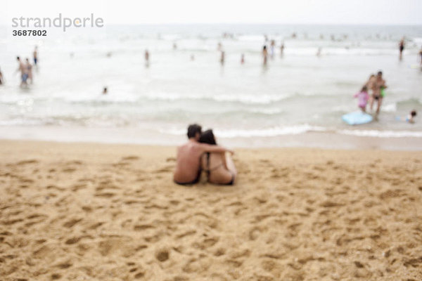 Ein Paar sitzt am Strand  defokussiert.