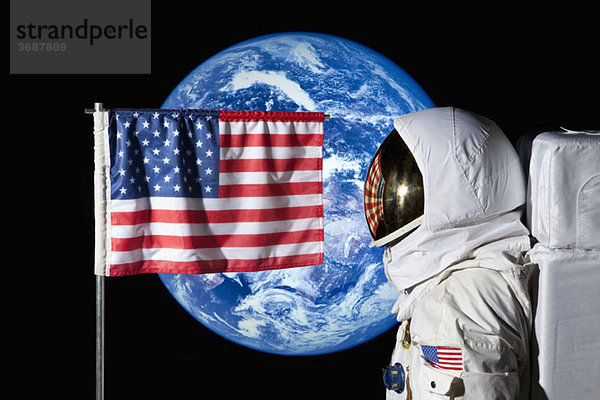 Ein Astronaut steht bei einer amerikanischen Flagge mit der Erde im Hintergrund.