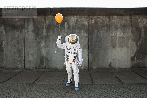 Ein Astronaut auf einem Bürgersteig  der einen Ballon hält.