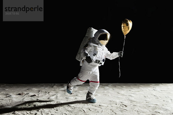 Ein Astronaut auf dem Mond hält einen herzförmigen Heliumballon.