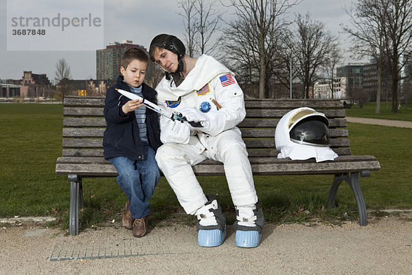 Ein Astronaut und ein Junge sitzen auf einer Parkbank und betrachten eine Modellrakete.