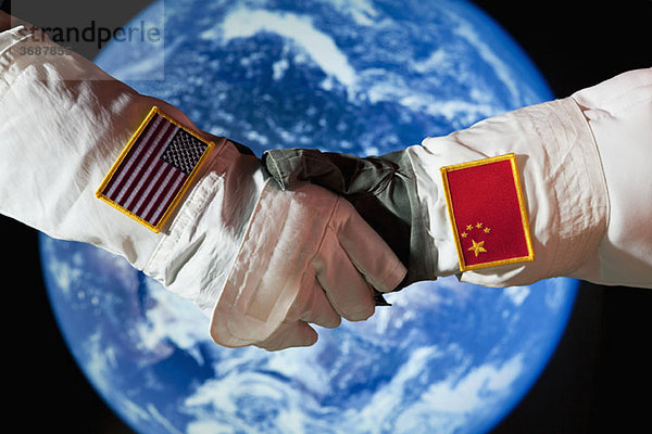 Ein amerikanischer Astronaut schüttelt einem chinesischen Astronauten die Hand.