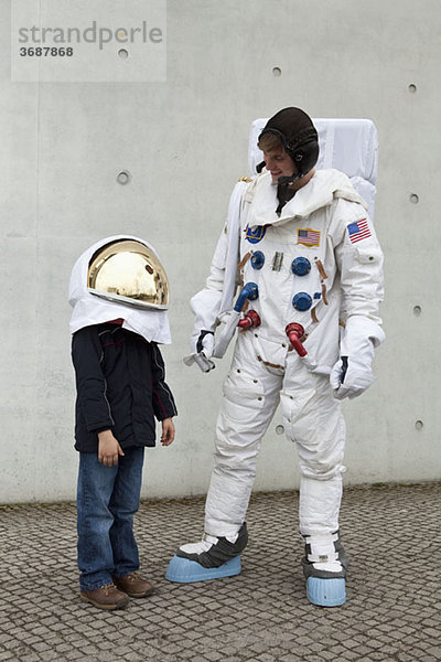 Ein Junge in einem Weltraumhelm schaut auf und steht neben einem Astronauten.