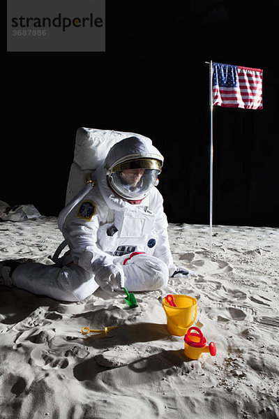 Ein Astronaut spielt mit einem Sandkübel und einer Schaufel auf dem Mond.