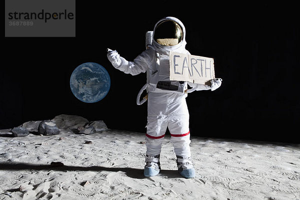 Ein Astronaut auf dem Mond mit ausgestrecktem Daumen  der das Zeichen'EARTH' hält.