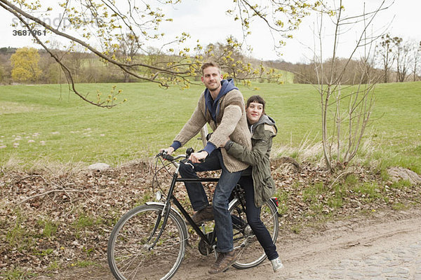 Ein Mann  der seine Freundin auf dem Land mit dem Fahrrad fährt.