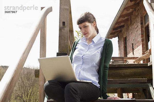 Eine Frau  die auf einer Treppe sitzt und auf einen Laptop schaut.
