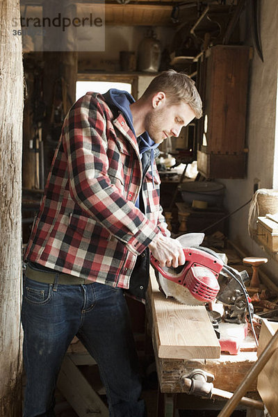 Ein Mann  der eine Kreissäge auf einem Brett in einer Werkstatt benutzt.