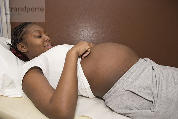 Eine schwangere Frau liegt auf einem Untersuchungstisch und lächelt auf den Bauch.