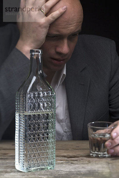 Ein betrunkener und depressiver Geschäftsmann mit einem Glas Wodka.