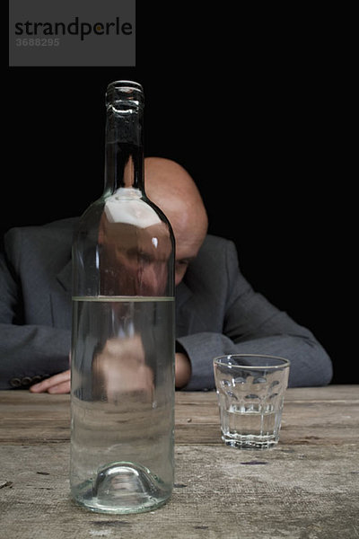 Ein betrunkener und depressiver Geschäftsmann mit einer Flasche Wodka und einem leeren Glas.