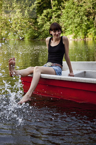 Eine junge Frau in einem Ruderboot  die mit dem Fuß ins Wasser spritzt.