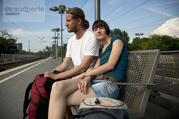 Ein gelangweiltes Backpacker-Paar  das auf einem Bahnsteig auf seinen Zug wartet.