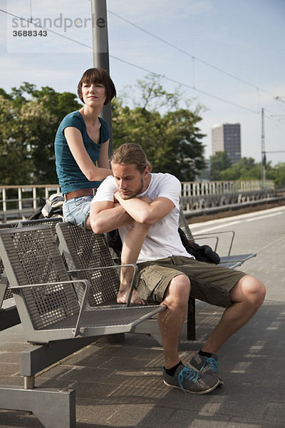 Ein gelangweiltes Backpacker-Paar  das auf einem Bahnsteig auf seinen Zug wartet.